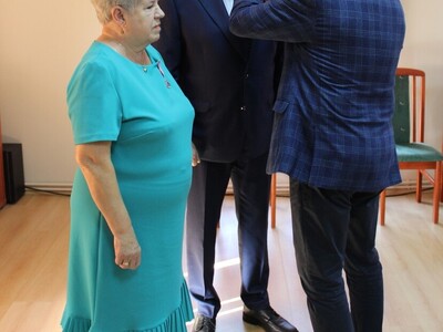 Wewnątrz. Trzy osoby stoją jedna przypina odznakę drugiej.