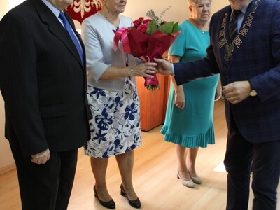Wewnątrz. Cztery osoby stoją. jedna wręcza kwiaty drugiej.