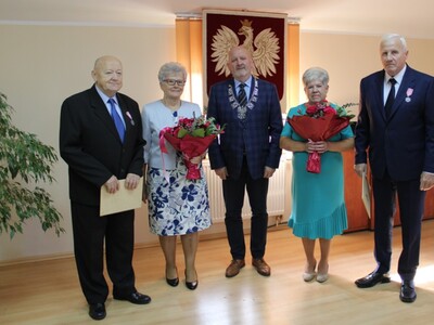 Wewnątrz. Pięć osób pozuje do zdjęcia z kwiatami i dyplomami.