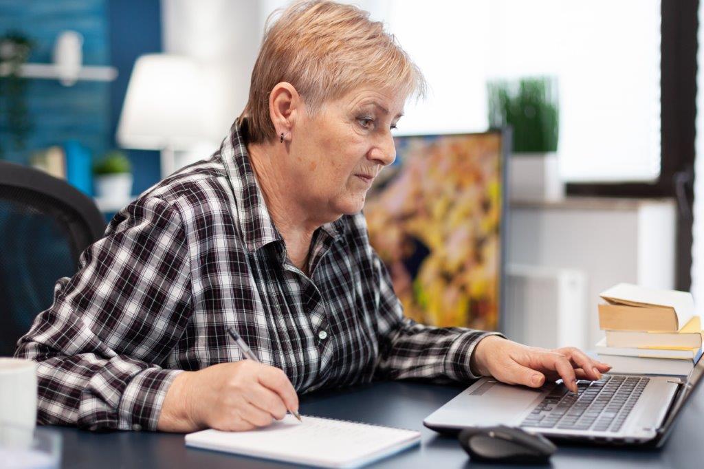 ZUS - kobieta zapisująca w notatniku oraz przeglądająca informacje w laptopie