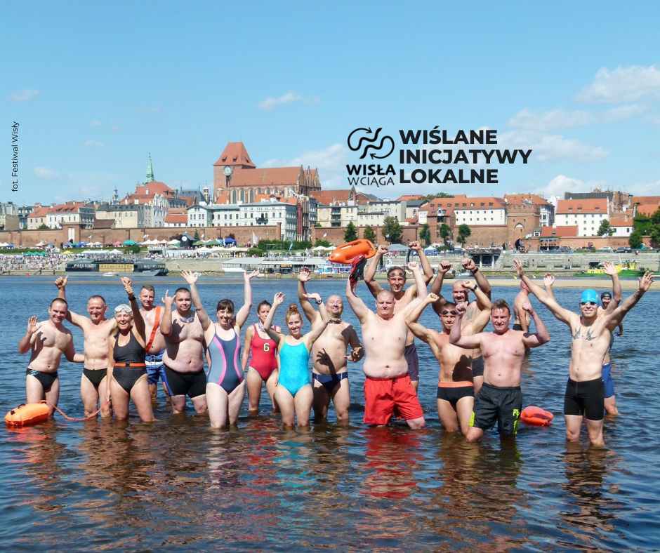 grupa osób w strojach kąpielowych stojąca w wodzie na tle miasta