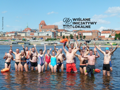 grupa osób w strojach kąpielowych stojąca w wodzie na tle miasta