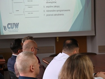 uczestnicy spotkania siedzą tyłem, w tle prezentacja dotycząca CUW