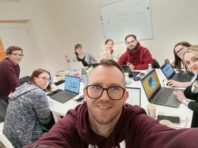na zdjęciu grupa nauczycieli w tracie kursu, na stole stoją komputery wokół siedzą ludzie
