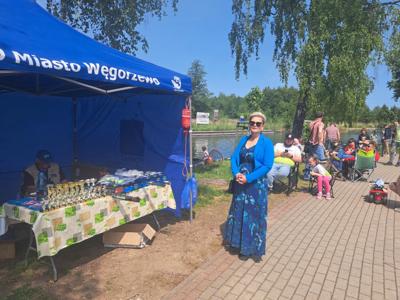 Starosta Węgorzewski w długiej, niebiesko-białej wzorzystej sukience i niebieskiej kurtce stoi na utwardzonej ścieżce. W tle niebieski namiot