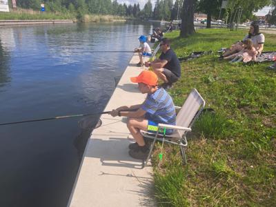 Dwie osoby łowią ryby nad spokojnym zbiornikiem wodnym z betonowego nabrzeża.