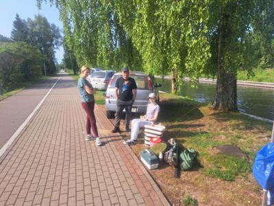 Trzy osoby znajdują się przy utwardzonej ścieżce obok trawiastego obszaru i zbiornika wodnego. 