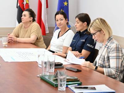 na zdjęciu uczestnicy spotkania, cztery panie siedzą przy stole w sali konferencyjnej w tle flagi