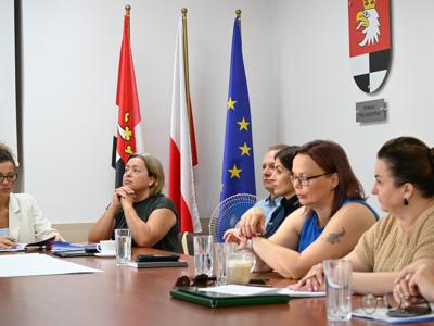 na zdjęciu uczestnicy spotkania, cztery panie siedzą przy stole w sali konferencyjnej, słuchają przemówienia