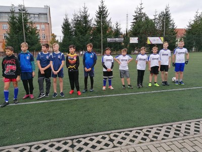 Zdjęcie grupowe zawodników. W tle boisko do gry w piłkę nożną oraz choinki.