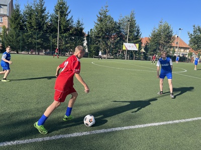 Zawodni SP 1 w Węgorzewie kopiący piłkę na połowę przeciwnika, na przeciw zawodnik z przeciwnej drużyny