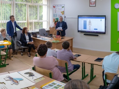 zaproszeni goście siedzą w ławkach w oddanej do użytki sali dydaktycznej  głos zabiera dyrektor SOSW w Węgorzewie tle tablica interaktywna