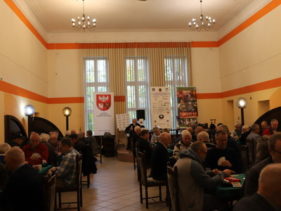 zawodnicy przy stołach w czasie trwających rozgrywek, w tle roll-up sponsorów