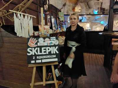 sztaluga z obrazem, na którym widnieje napis ,,sklepik z rękodziełem" obok stoi kobieta
