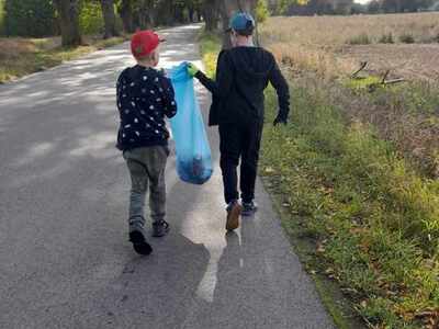 dwoje chłopców idzie droga w ręku trzymając worek ze śmieciami 