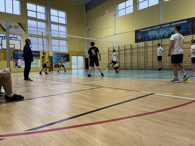 dwie drużyny rywalizują pod siatką na boisku obok stoi sędzia