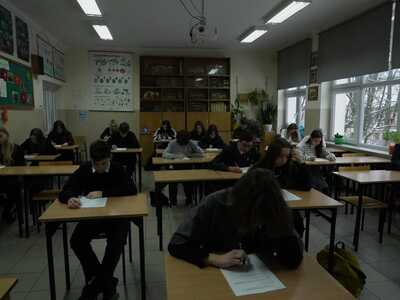 uczestnicy podczas pisania testu - siedzą w ławkach w sali lekcyjnej 