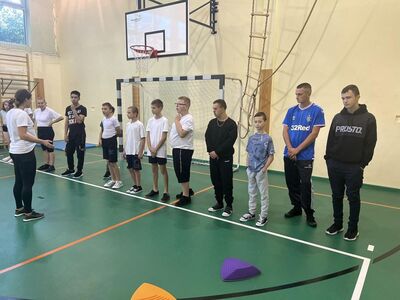 na zdjęciu uczniowie w strojach sportowych, w tle bramka 