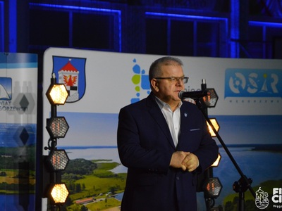 Na scenie Burmistrz Węgorzewa przemawia do mikrofonu, w tle baner gminy Węgorzewo