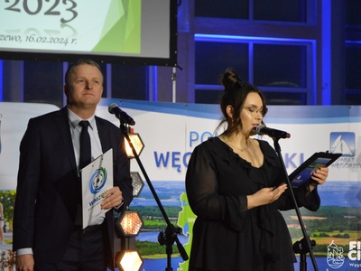 Prowadzący galę stoją na scenie przy mikrofonach w tle baner powiatu węgorzewskiego 