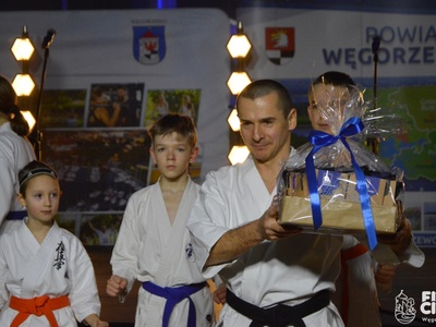 Trener zespołu Kyokushin Karate trzymający pakiet promocyjny powiatu węgorzewskiego w tle dzieci
