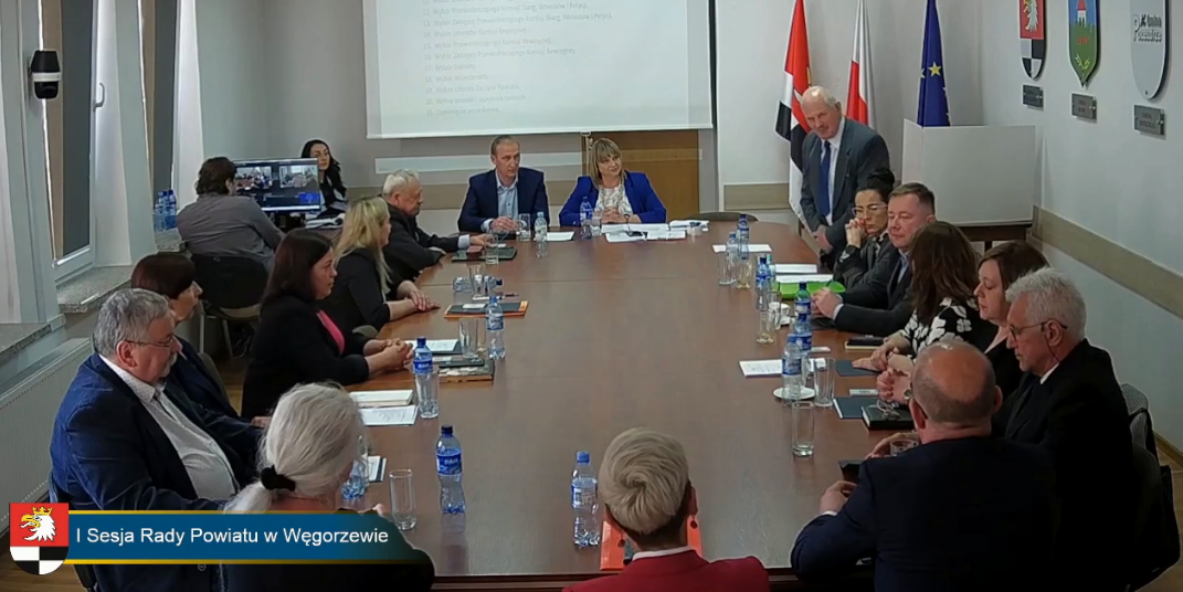 sesja - na zdjęciu radni przy stole w tle rzutnik oraz flagi