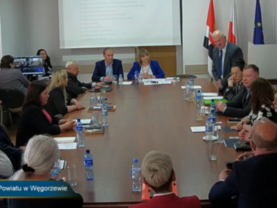 sesja - na zdjęciu radni przy stole w tle rzutnik oraz flagi
