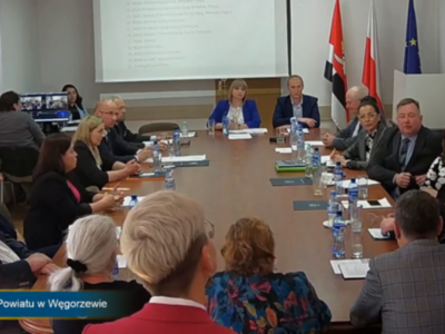 sesja - na zdjęciu radni przy stole w tle rzutnik oraz flagi