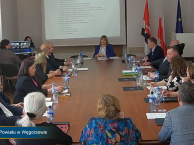 sesja - na zdjęciu radni przy stole w tle rzutnik oraz flagi