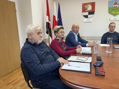 na zdjęciu cztery - główny spec. ds. bezpieczeństwa i zarządzania kryzysowego, starosta węgorzewski, wicestarosta osoby w tle flagi, herb powiatu

