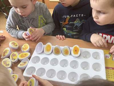 na zdjęciu troje chłopców  podczas zabawy grą edukacyjną, w tle meble