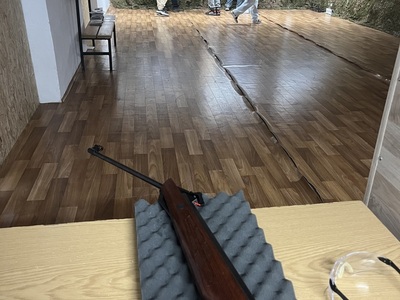 na pierwszym planie broń w tle zawodnicy przy tarczach 