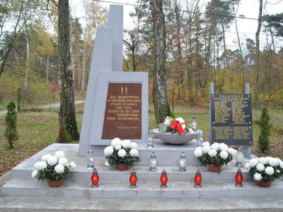 pomnik upamiętniający poległych żołnierzy  w obronie niepodległości Polskiej, na pomniku kwiaty w kolorze białym i czerwonym oraz palące się znicze w kolorze czerwonym 