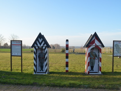 dwie budki wartownicze stylizowane na czasy zaborów budka zaboru pruskiego oraz budka zaboru rosyjskiego, po środku słup graniczny a po bokach dwie tablice opisujące ważne wydarzenia na terenie miejscowości Ostrów Kaliski 