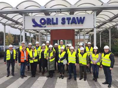 przedstawiciele Gminy Brzeziny w kamizelkach odblaskowych i kaskach przed wejściem do ZUOK "Orli Staw"