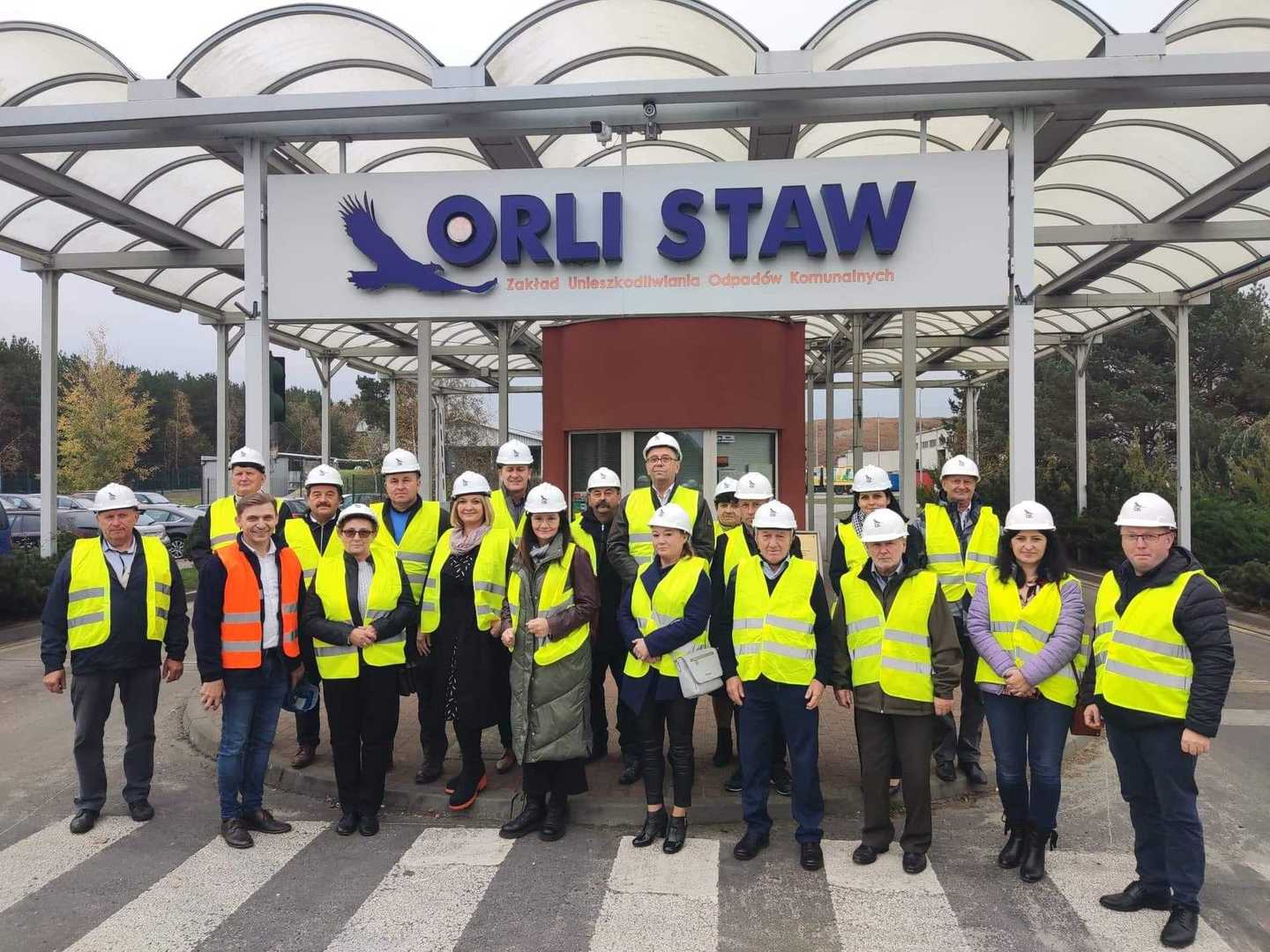 przedstawiciele Gminy Brzeziny w kamizelkach odblaskowych i kaskach przed wejściem do ZUOK "Orli Staw"