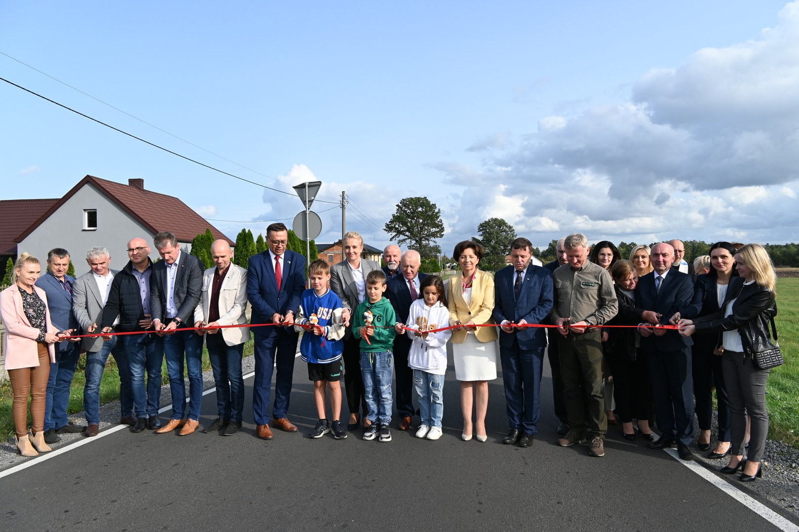 goście przecinający wstęgę na drodze