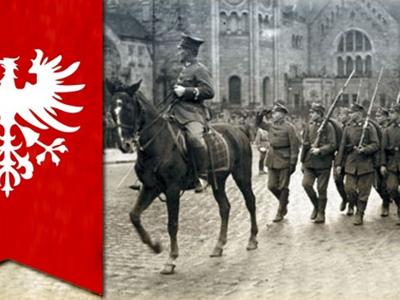 Historyczna fotografia żołnierzy maszerujących ulicą obok jeźdźca na koniu, obok czerwony sztandar z białym orłem.
