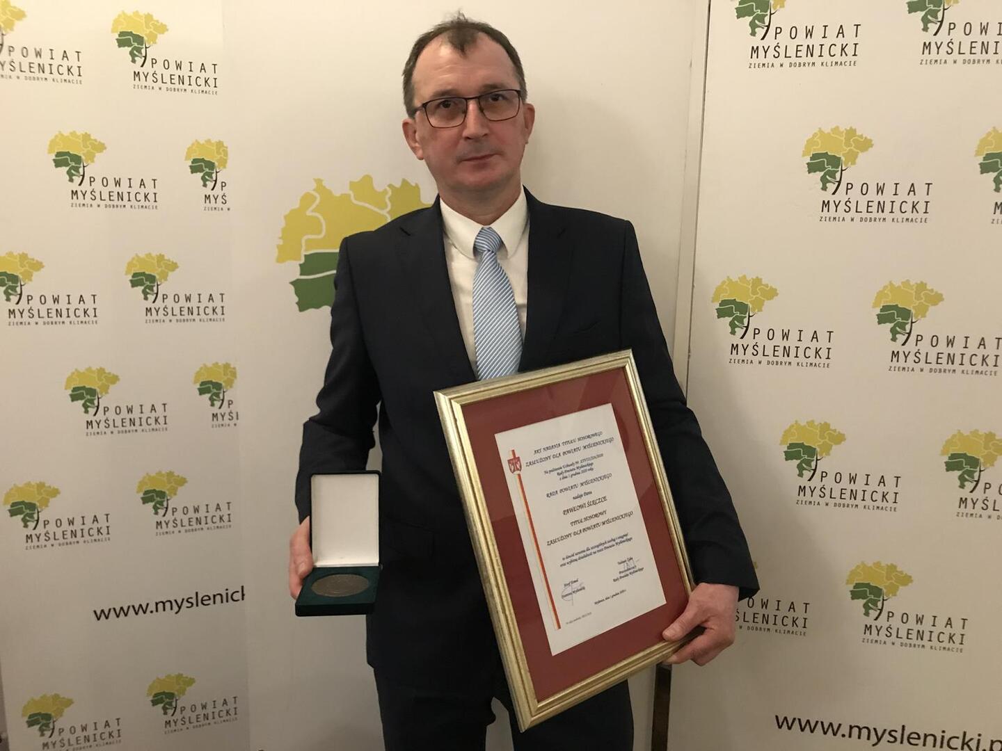 Na zdjęciu widoczny laureat „Zasłużony dla Powiatu Myślenickiego”, na tle logo Powiatu Myślenickiego
