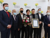 Rodzina laureata, w tym przedstawiciele Powiatu Myślenickiego, pozują wspólnie na tle ścianki z logo Powiatu Myślenickiego.