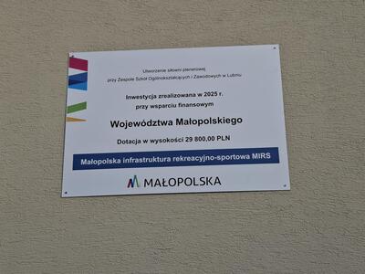 Tablica informacyjna na ścianie budynku informująca o dofinansowaniu siłowni z Wojew&oacute;dztwa Małopolskiego