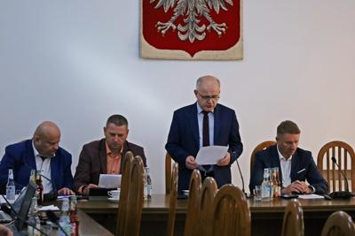 Starosta Józef Tomal oraz trzech Radnych siedzą przy stole. Przewodniczący Tadeusz Żaba stoi, czyta dokument. W tle herb Polski.
