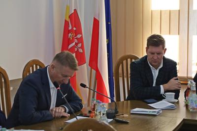 Starosta Józef Tomal i Radny Kamil Ostrowski siedzą przy stole z mikrofonami. W tle flagi Polski, Unii Europejskiej i powiatu.