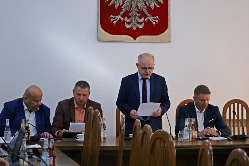 Starosta Józef Tomal oraz trzech Radnych siedzą przy stole. Przewodniczący Tadeusz Żaba stoi, czyta dokument. W tle herb Polski.