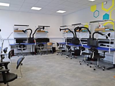 Nowoczesna pracownia komputerowa z zestawami do pracy przy elektronice i wentylacją stanowisk.