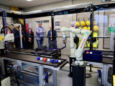 Stanowisko z robotem przemysłowym w pracowni robotyki, w tle obserwujący goście.