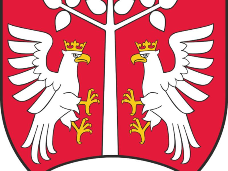 Herb powiatu myślenickiego: dwa białe orły w koronach po bokach białego drzewa na czerwonym tle, u dołu biały półokrąg.