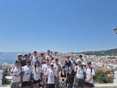 Uczestnicy projektu Erasmus+ pozują na tarasie z widokiem na białe zabudowania greckiego miasta i morze.