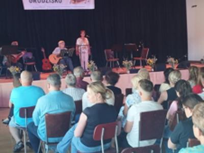 Widownia oglądająca występ wokalistki i gitarzysty na scenie podczas Festiwalu Piosenki Beskidzkiej „Grodzisko”; w tle baner wydarzenia.