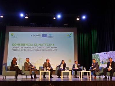 Na scenie siedzi siedmioro prelegentów biorących udział w panelu dyskusyjnym podczas konferencji klimatycznej.